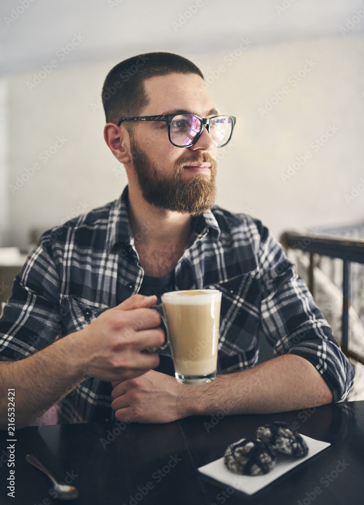 Smiling bearded man in glasses holding a glass with coffee Smiling bearded man in glasses holding a glass with coffee