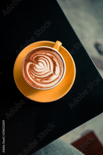 Flat white coffee in yellow cup on black table at the hipster coffee shop. Latte art concept. Dark food photo. Vintage color tones, filter effect. Copyspace
