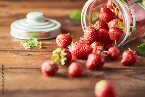 Fresh Healthy strawberry falls out from glass jar over wooden background.