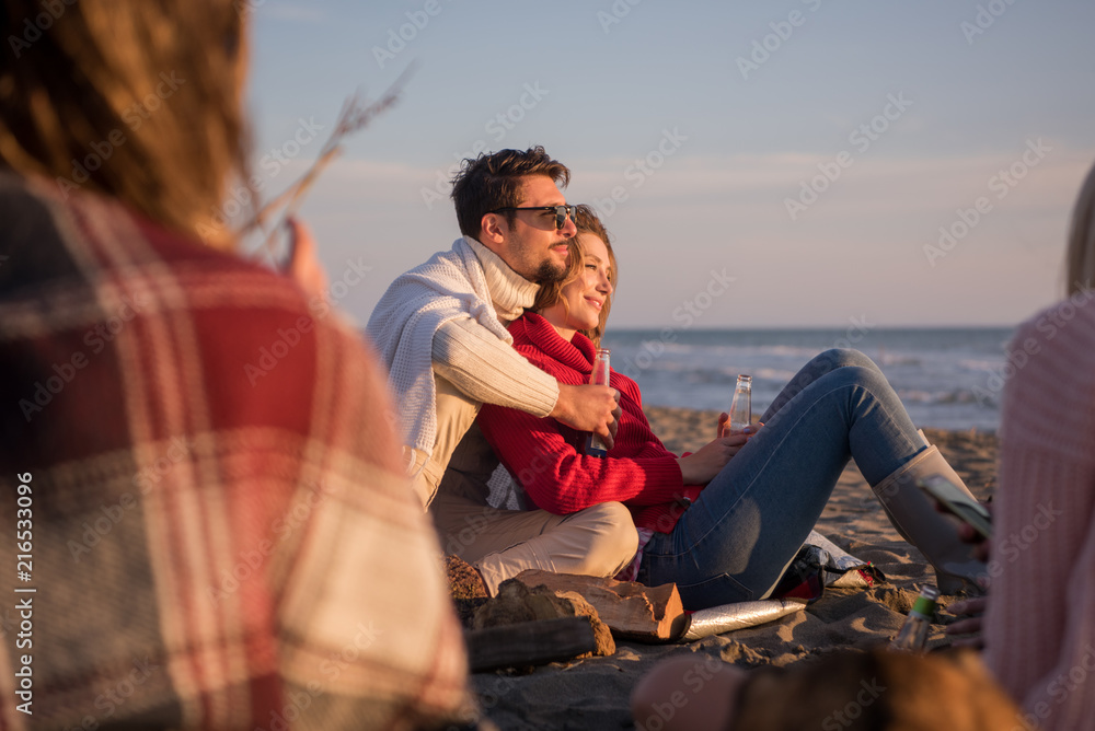 Fototapeta premium Couple enjoying with friends at sunset on the beach