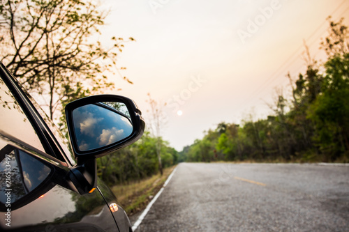 Side mirror of a car which parked on a side of the empty road.