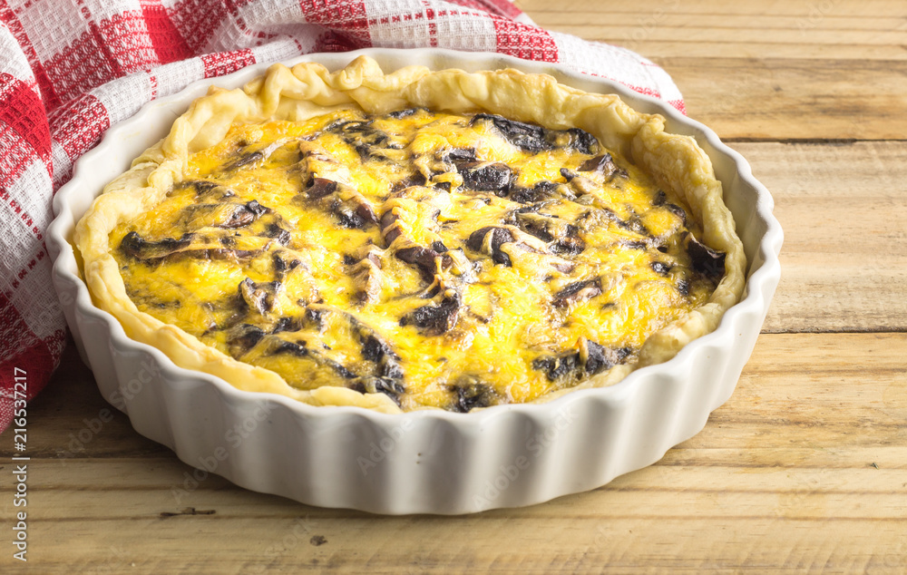 Mushroom tart on rustic wooden kitchen table - Side view photo of mushroom and cheese quiche dish Mushroom tart on rustic wooden kitchen table - Side view photo of mushroom and cheese quiche dish
