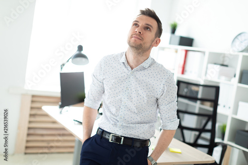 A young man stands leaning on a table in the office. photo