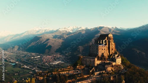 Aerial: drone flying at old medieval abbey perched on mountain top, snowy Alps at sunrise. Sacra di San Michele (italian) - Saint Michel Abbey (english traslation) - Turin, Italy photo