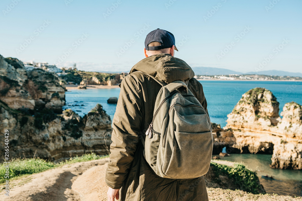 A tourist or traveler with a backpack admires the beautiful view of the Atlantic Ocean and the coast near the city called Lagos in Portugal.