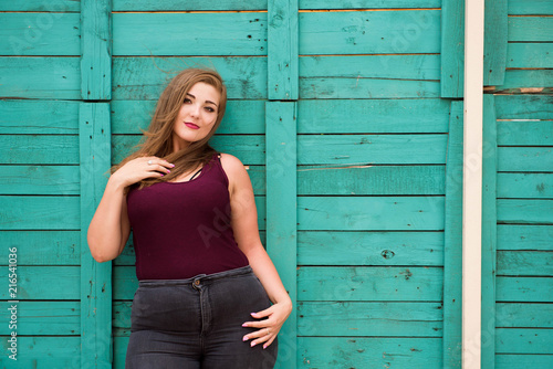 Beautiful woman wearing ripped jeans standing against cafe wall on city street. Casual fashion, elegant everyday look. Plus size model. photo