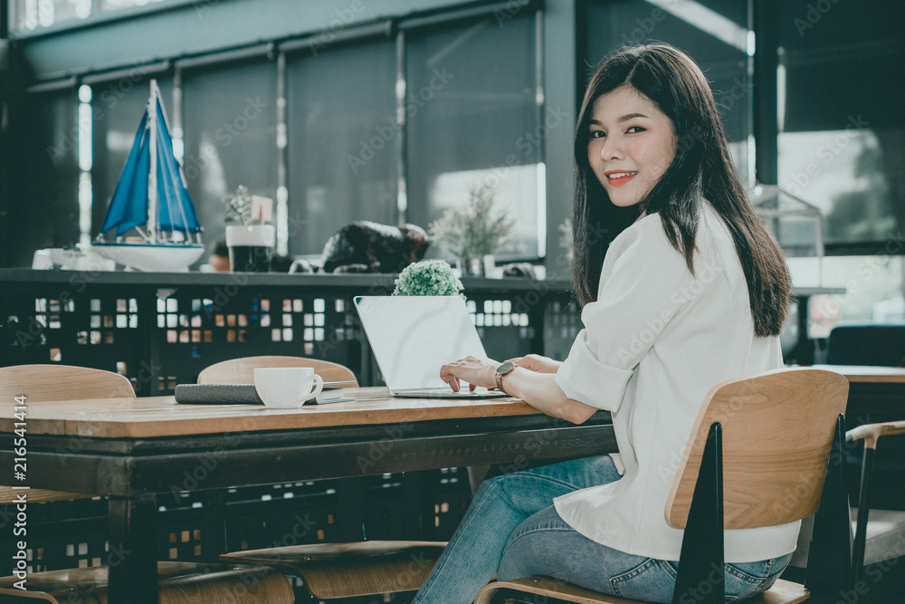 Obraz premium An Asian girl is freelancer woman, she is working by using the laptop computer and drinking a cup of coffee on morning in a coffee shop or her office.