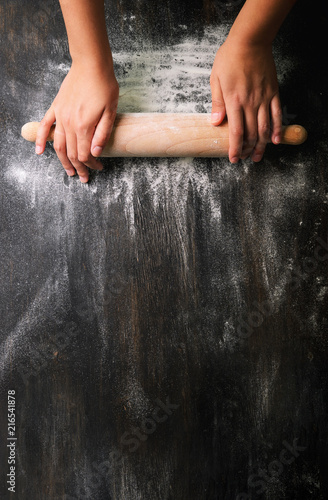 Girl hands keep rolling pin with flour on dark black table, baking background, top view, copy space for your text, meru, recipe. Banner