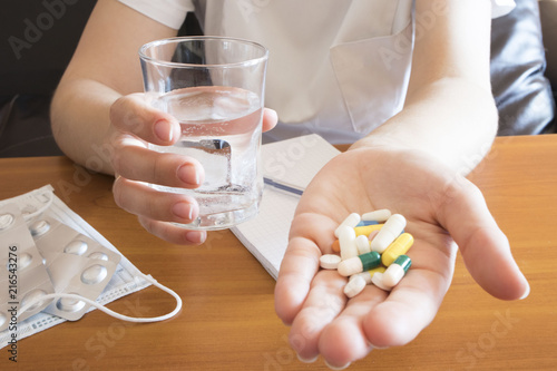 Pills, tablets and drugs heap in doctor hand and glass of water, closeup view