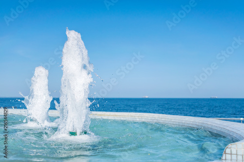 The gush of water of fountain. Splash and Foam of water. Blue vertical fountain with mosaic pool on the wooden terrace, by the sea. Rest on the beach, sea freshness in the summer heat. 