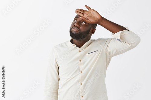 Phew, it was close. Upset and tired handsome young African American in white shirt, whiping sweat out of forehead, hazing at upper left corner with normal expression, work finished, resting photo