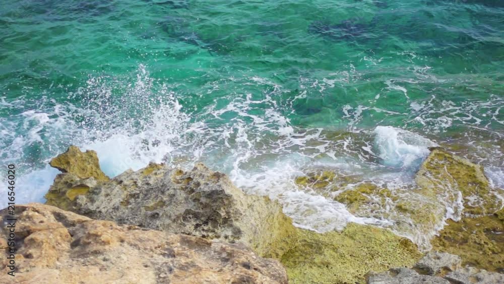 Aerial ocean view of turquoise sea at sunny day. Top view of seawater waves splashing against old moldy rocks in slow motion Aerial ocean view of turquoise sea at sunny day. Top view of seawater waves splashing against old moldy rocks in slow motion