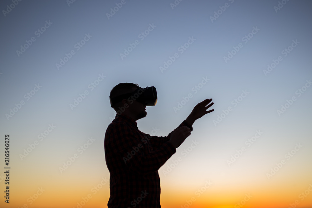 Future has come. Man wearing virtual reality goggles on the sky background