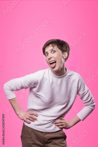 Studio portrait on pink background of young caucasian girl with its tongue hanging out.