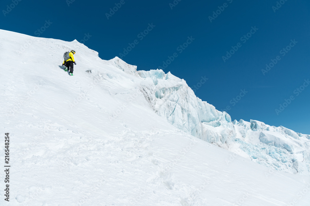 A skier in a helmet and mask with a backpack rises on a slope against the background of snow and a glacier. Backcountry Freeride