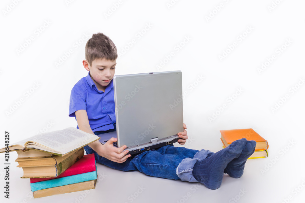 Portrait of cute schoolboy sitting with books and typing on laptop keyboard Portrait of cute schoolboy sitting with books and typing on laptop keyboard