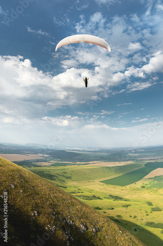 White orange paraglide with a paraglider in a cocoon against the background of fields of the sky and clouds. Paragliding Sports