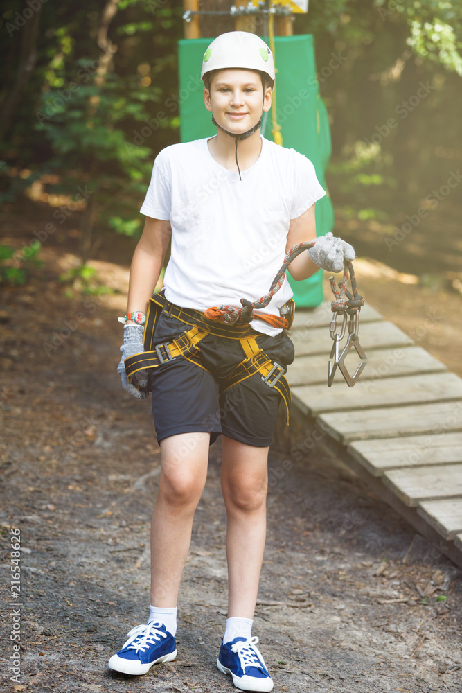 Happy, cute, young boy in white t shirt and helmet having fun and playing at the adventure park, holding ropes and climbing wooden stairs. Hobby, active lifestyle concept Happy, cute, young boy in white t shirt and helmet having fun and playing at the adventure park, holding ropes and climbing wooden stairs. Hobby, active lifestyle concept