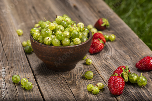 ripe gooseberry in a plate and strawberries in a garden on a table