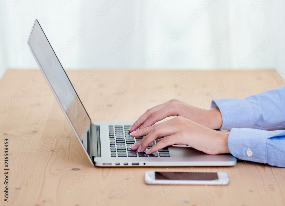 Fototapeta premium Woman hands typing on laptop keyboard at the office, Woman worker and business concept, Soft focus on vintage wooden table.