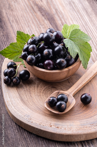 Fresh ripe black currant in wooden bowl with original leaves on rustic old background