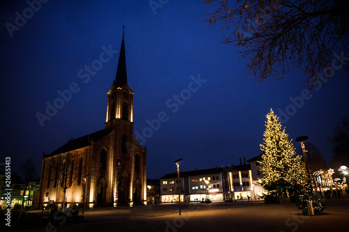 Calm City with illuminated german evangelical church during the winter Christmas holidays in central Kehl, Baden-Wurttemberg, Germany with Christmas Tree and pedestrians silhouettes