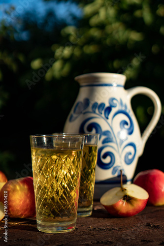 Traditional apple wine in the city of Frankfurt in Hesse. A jug of wine is on an old wooden table in the garden, around it are apples