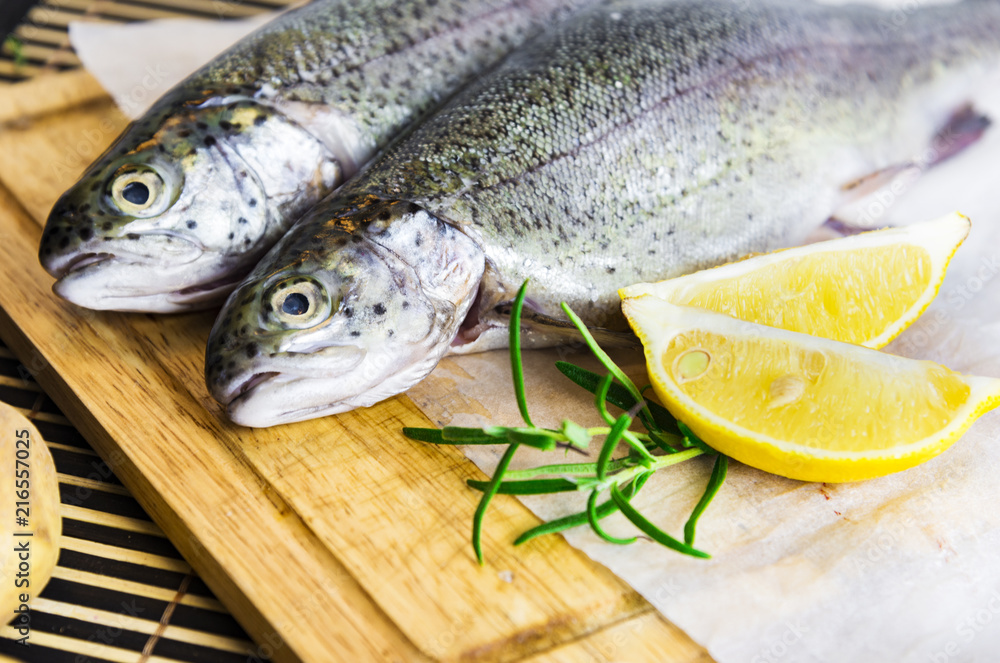 A table with a cutting board with fresh trout, slices of lemon and rosemary on the side A table with a cutting board with fresh trout, slices of lemon and rosemary on the side