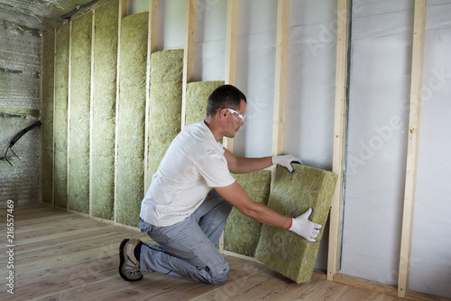 Fotografie Worker in protective goggles and respirator insulating rock wool insulation in wooden frame for future house walls for cold barrier
