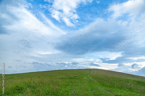 Green grass hills landscape in summer against blue sky and white clouds.