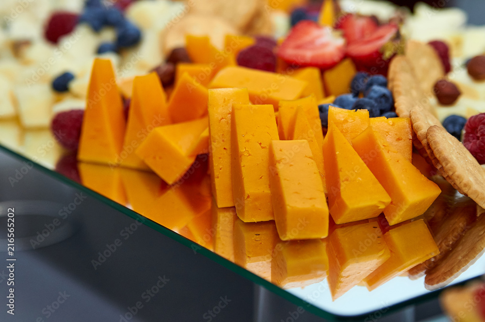 A dish for a buffet. Appetizing, tasty, expensive food for snacks. Large pieces of cheese, crackers, grapes, blueberries, strawberries, raspberries and other berries.