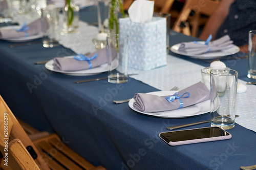 The table awaits guests for the celebration of a birthday, a wedding, christening, the birth of a child. Someone forgot his phone on the festive table.