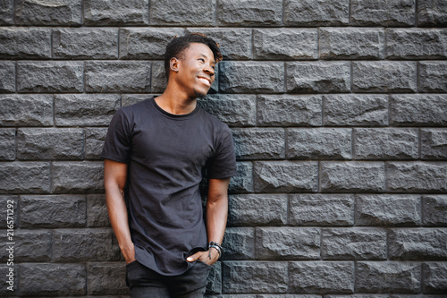 African american fashion male model in blank black t-shirt standing against brick wall