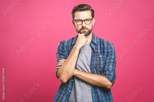 Fotografia Portrait of unhappy determined european male with bristle touching chin while thinking and looking with serious and worried look at camera, standing against pink background