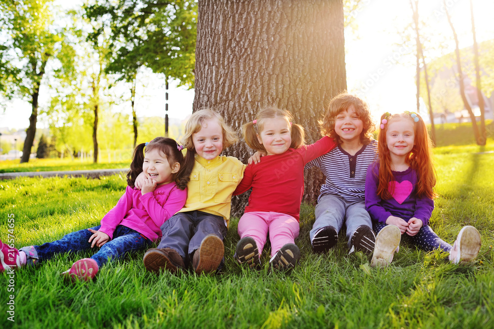 Fototapeta premium group of happy little children smiling sitting in park on grass under a tree. June 1, Children's Day, friendship, childhood, vacation.