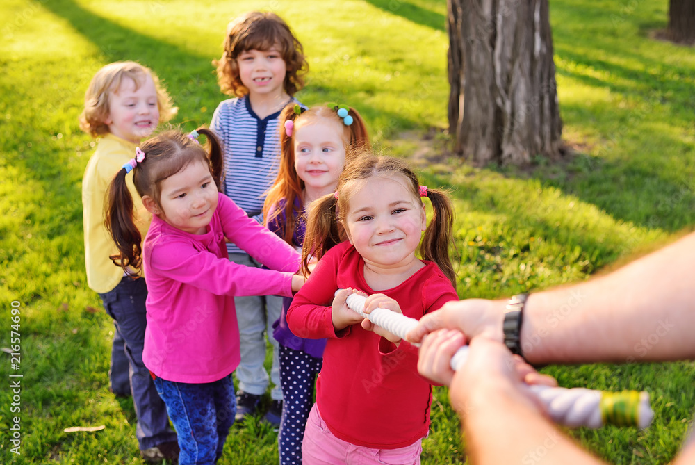 Fototapeta premium Children play tug of war in the park. Children's Day, June 1, friendship, childhood, vacation, camp