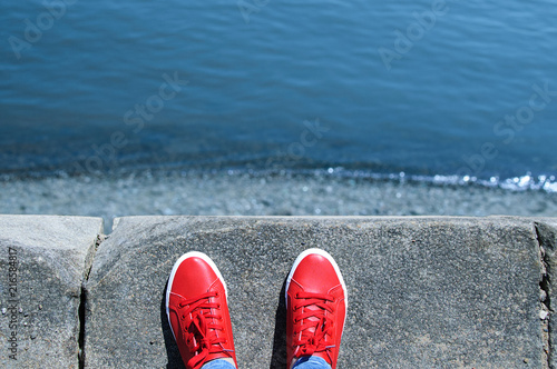 Legs in red sneakers stand on the edge. View of the sea.