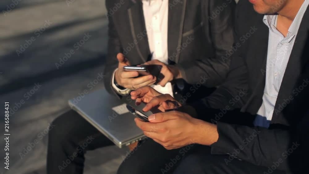 two businessmen working with phones sitting on a bench two businessmen working with phones sitting on a bench