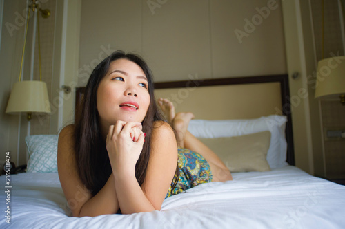 young beautiful and happy Asian Chinese Korean lying on bed in the morning at home bedroom or hotel room feeling cheerful and relaxed smiling playful