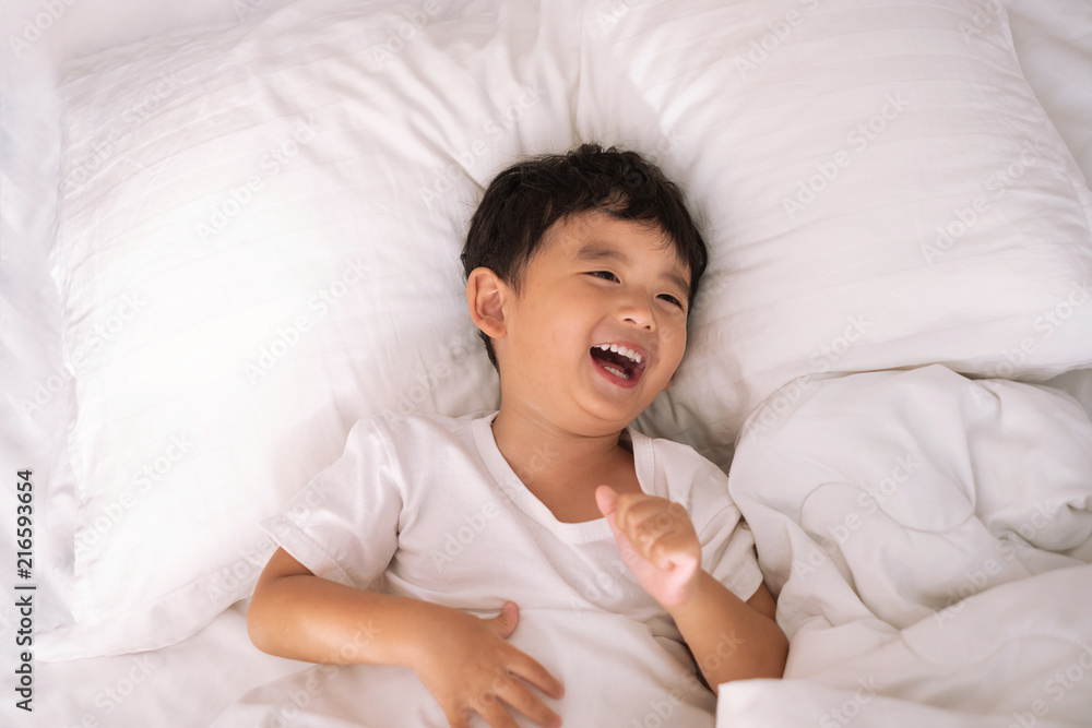3 years old little cute Asian boy at home on the bed, kid lying playing and smiling on white bed with pillow and blanket, top view with copy space. 3 years old little cute Asian boy at home on the bed, kid lying playing and smiling on white bed with pillow and blanket, top view with copy space.