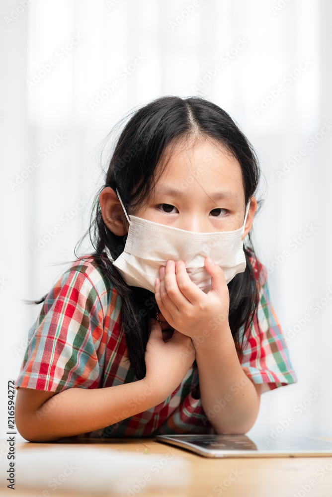 Asian girl wearing white mask and playing tablet at home. Asian girl wearing white mask and playing tablet at home.