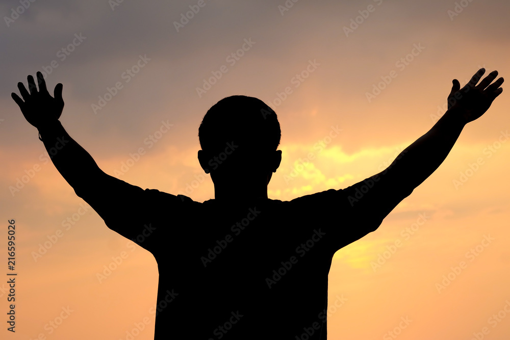The silhouette of a man spread his arms wide as a winner or freedom on sunset  background