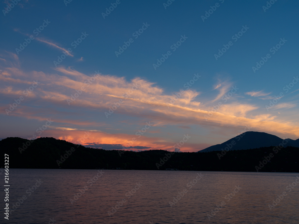 夕焼の湖畔にて、青い空に筋雲がオレンジ色に染まり湖面に映す。