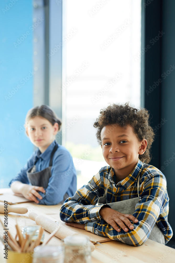 Fototapeta premium Mixed-race pupil and his classmate sitting by desk at lesson of craftsmanship