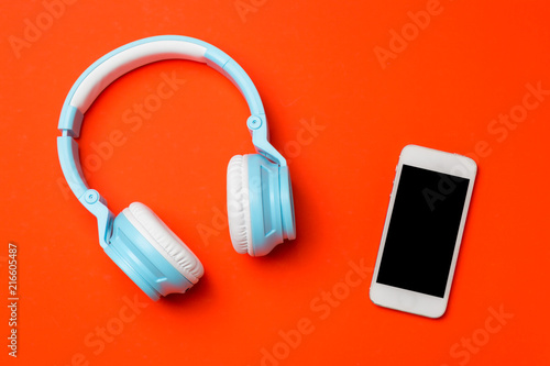 Blue modern wireless headphones with a mobile phone on red orange background. Listening to music concept.