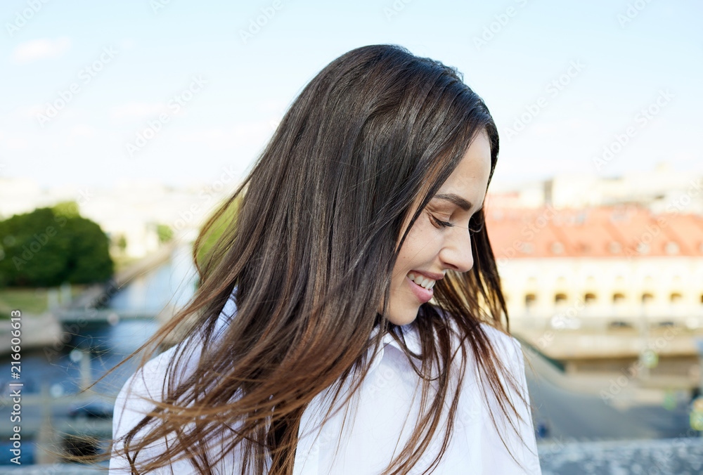 Happy beautiful girl with black hair keeping eyes closed while feeling wind and enjoying weather in city