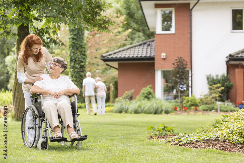 Nurse supporting disabled senior woman in the wheelchair in the garden Nurse supporting disabled senior woman in the wheelchair in the garden