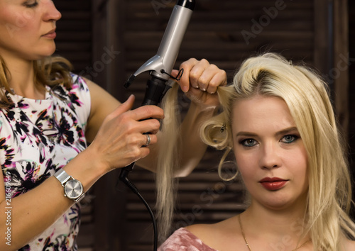 Hairdresser does hairstyle for luxurious blond woman. coiffure in the form of big curl. Concept wedding hairstyle