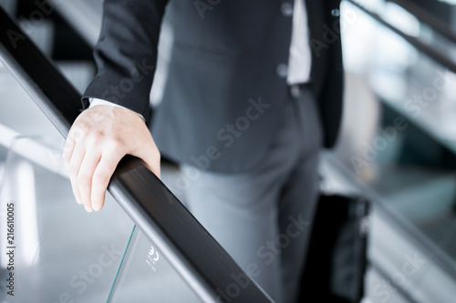 Hand of young businessman on railings of escalator during motion downwards