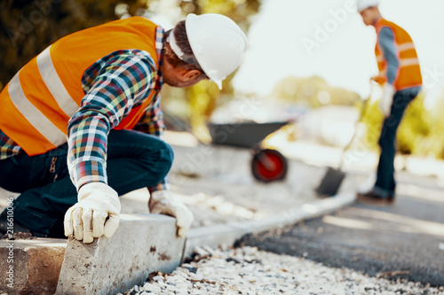 Worker with gloves and in helmet arranging curbs on the street photo